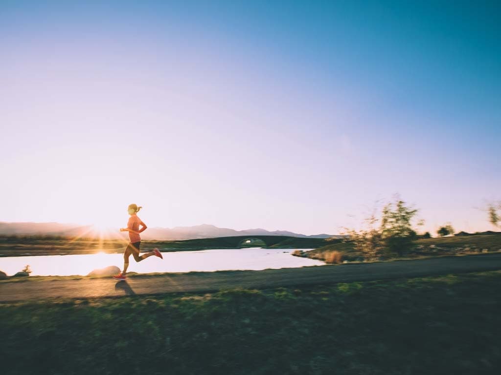 Běžec běží po sluncem zalité cestě, obklopený zelení a jasným světlem