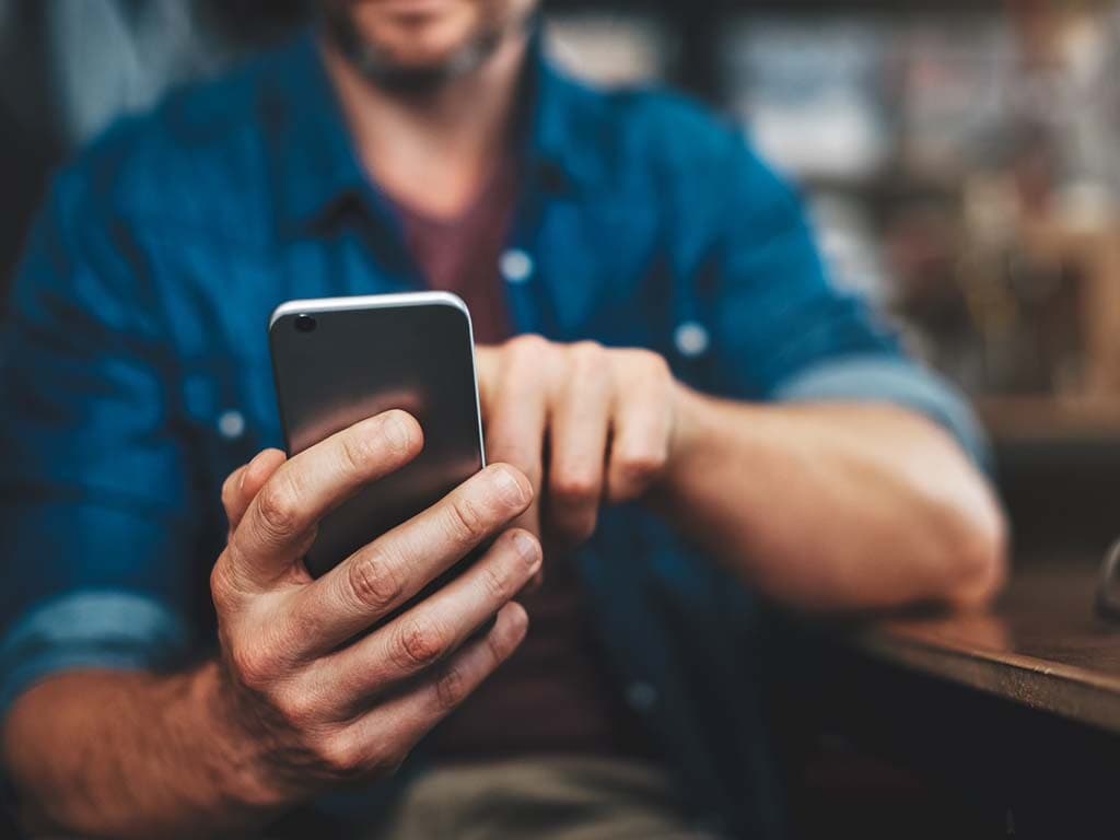 Muž sedí u stolu a soustředí se na svůj mobilní telefon, buď konverzuje, nebo prohlíží obsah