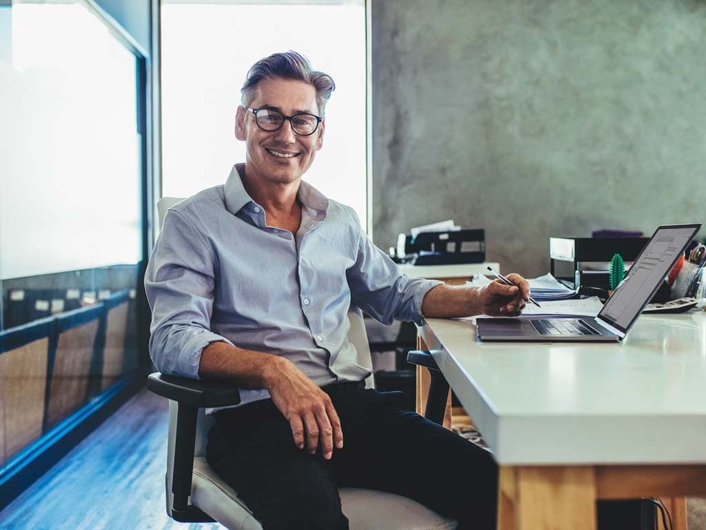 Muž v supermarketu drží mobilní telefon a prohlíží si zboží na regálech kolem sebe