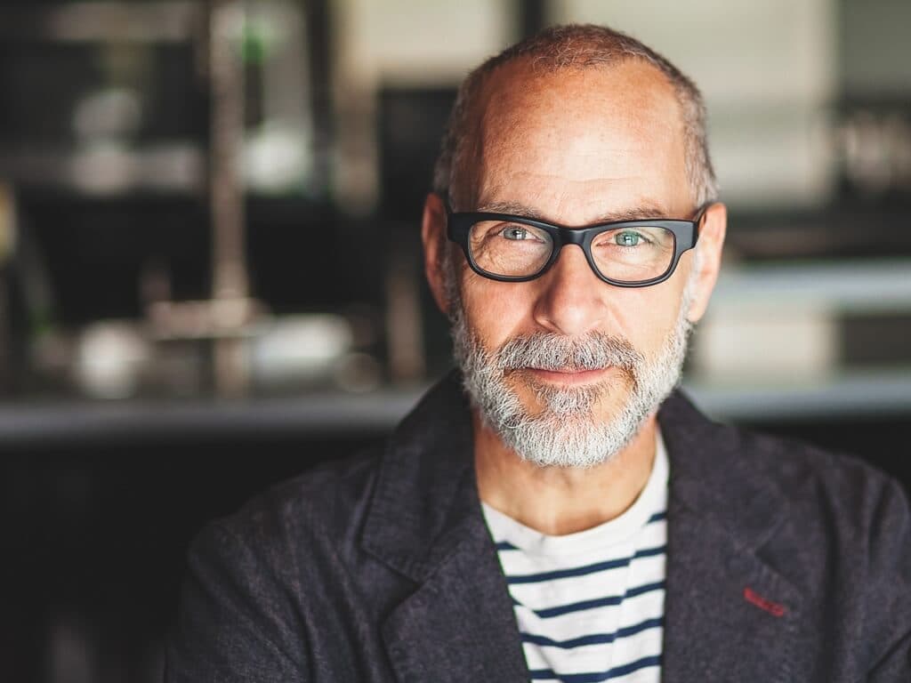 Muž s brýlemi a vousy, který zamyšleně hledí do strany